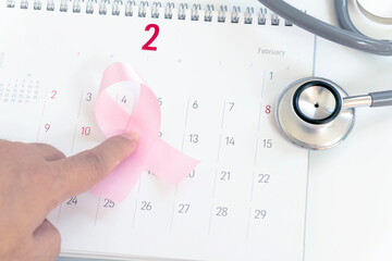 woman holding in hands pink breast cancer sign on white background calendar and stethoscope.