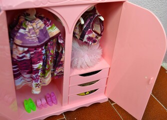 Detail shot of a pink doll's wardrobe with drawers, hanging clothes and several pairs of shoes lined up