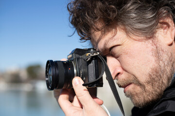 Fototapeta premium caucasian photographer with blond beard taking pictures with a retro 35mm black camera outdoors