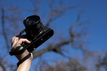 Fototapeta premium photo from below holding a 35mm camera with a blue sky background and trees in winter