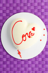 A cake in heart shape.  Mousse light cake in the shape of a heart with the inscription on a purple background. Valentine's Day. Vertical photo