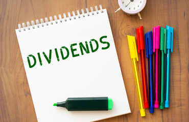 A notebook with the text DIVIDENDS lies on a brown wooden table.