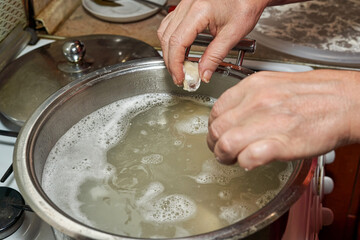 Hands put raw dumplings in boiling water