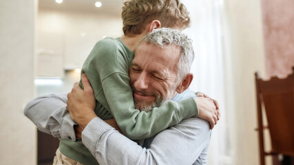 The love of grandpa. Happy grandfather embracing his cute little preschool grandson while standing...