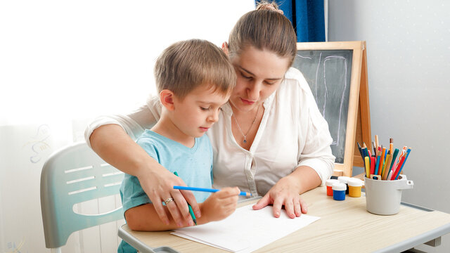 Mother teaching drawing and writing her little son. Boy learning writing with pencil at home Concept of education and remote school at home during lockdown and self isolation.