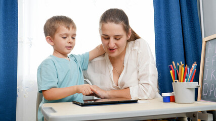 Happy little boy with mother playing on tablet computer after studying and learning at home. Digital tablet computer and gadgets at education. Remote school during lockdown