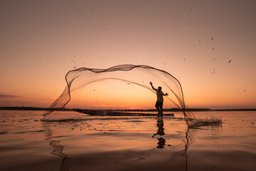 Asian fisherman on wooden boat casting a net for catching freshwater fish in nature