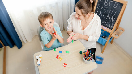 Top view photo of boy with mother shaping and sculpting colorful plasticine and clay. Family having fun with colorful toy dough