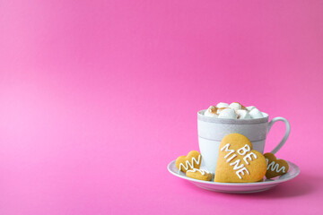 Cup of hot tea or coffee with marshmallow and cookie in heart shape with Be Mine phrase on pink background. Romantic breakfast on Valentines Day, Merriage, Engagement or Dating concept.