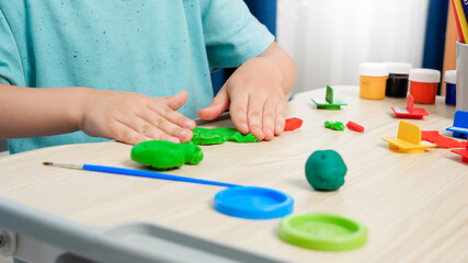 Fototapeta na wymiar Closeup of little boy forming and shaping colorful plasticine or clay with hands. Special colorful dough for enhancing children motor skills. Child education, creativity and art.