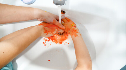 Closeup of little boy washing colorful paint off his hands after drawing with fingers. Concept of...