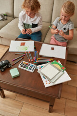 High angle view of adorable little children, boy and girl drawing on paper using marker pen, sitting together on a couch at home