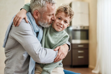 Hug time. Happy grandfather embracing his cute little preschool grandson while standing together at...