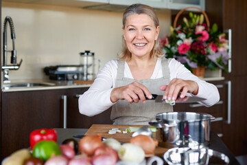 Senior woman in the kitchen cooking, mixing food in a pot.