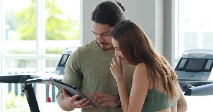 Handsome personal trainer gives advice to sporty woman at fitness gym.