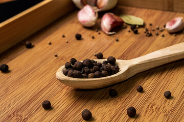 Allspice in a wooden spoon on a wooden background. Garlic and bay leaf. View from above. Seasoning flavoring for meat and food..