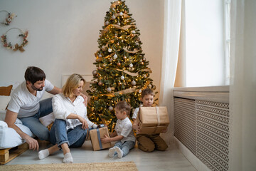 happy caucasian family sitting next to christmas tree  by the window with presents under it. Christmas morning