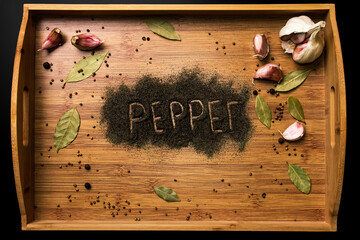Ground black pepper with a wooden inscription "Pepper" on a wooden background. View from above. Garlic and bay leaf on the background. Seasonings for meat and spicy dishes..