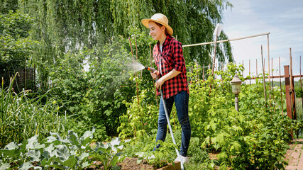 Smiling young girl holding water hose watering growing vegetables at backyard garden