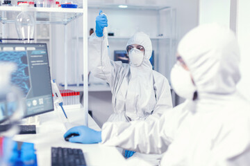 Woman scientist in coverall using micropipette in lab for coronavirus research. Team of...