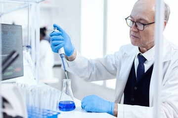 Experienced scientist working in biotechnological laboratory with sterile dropper and blue liquid....