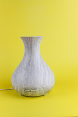 Grey aroma diffuser with steam from water and oil on yellow background