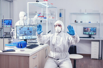 Virolog dressed in ppe suit developing coronavirus vaccine on digital screen making hand gesture. Medical scientist using modern technology to cure diseases and develop a cure.