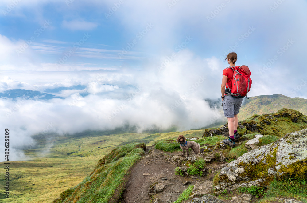 Canvas Prints A female hiker and their dog at the viewpoint from the summit of Meall Garbh near a cloudy Loch Tay and Killin villiage in the Scottish Highlands, UK.