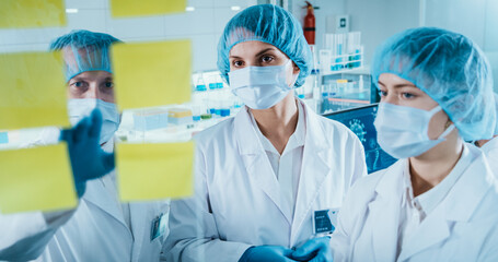 COVID-19 - diverse laboratory team. Looking at glass wall with adhesive notes