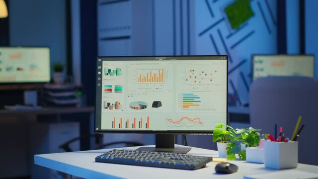 Interior of empty start up business office with modern design during night with graphics running on the desktop. Financial company with nobody in it, place of work startup, workplace indoors concept