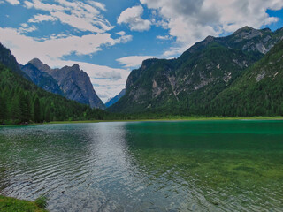 Blick über den Toblacher See in Südtirol an einem sonnigen Tag mit weissen Wolken auf blauem Himmel und Bergpanorama im Hintergrund