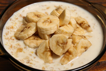 Oats porridge with banana slices in bowl over wooden background. Diet healthy nutrition food concept. Top view, flat lay