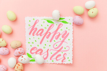 Happy Easter concept. Inscription HAPPY EASTER letters candy chocolate eggs and jellybean sweets isolated on trendy pastel pink background. Simple minimalism flat lay top view copy space.