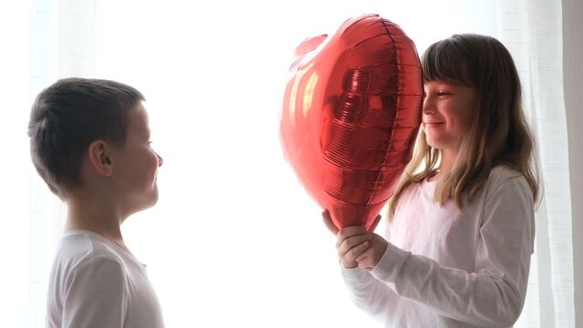 Cute, cute boy and girl are having fun with heart balloons, kissing a huge heart. Valentine's day, a holiday for all lovers. Slow motion