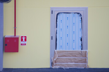 Yellow wall, with new entrance door still with protective seals and red box with hydrant attachment...