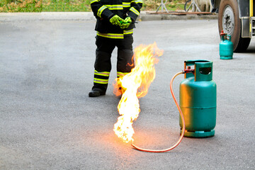 Fire burning on green gas container with Firefighter or fireman in black uniform and wheel background during fire safety training and copy space. Dangerous and Protective carrier concept. 