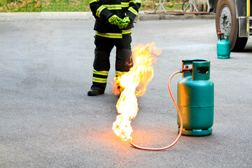 Fire burning on green gas container with Firefighter or fireman in black uniform and wheel...