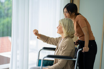 Obraz premium Senior old Caucasian patient on wheelchair with mixed race adopted daughter caring in the bed room. 