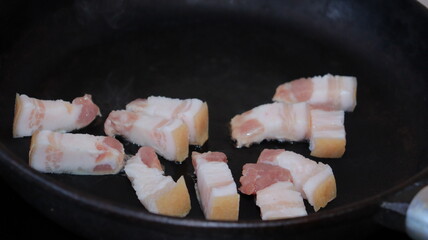 Fried pieces of bacon in a black pan.Pork belly close-up.