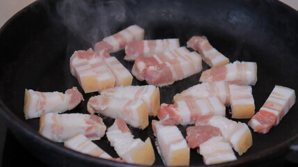 Fried pieces of bacon in a black pan.Pork belly close-up.