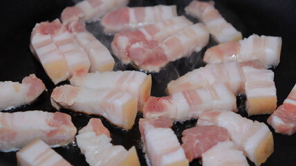 Fried pieces of bacon in a black pan.Pork belly close-up.