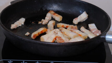 Fried pieces of bacon in a black pan.Pork belly close-up.