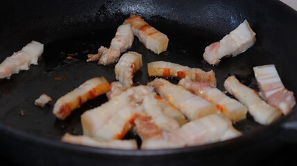 Fried pieces of bacon in a black pan.Pork belly close-up.