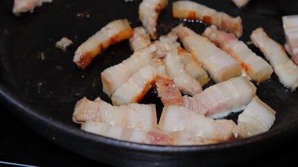 Fried pieces of bacon in a black pan.Pork belly close-up.