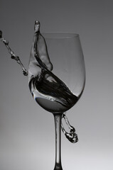 Wine glass and splash of liquid on an grey background, drops.