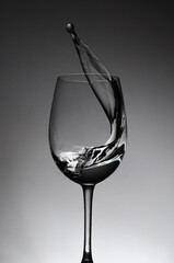 Wine glass and splash of liquid on an grey background, drops.