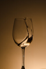 Wine glass and splash of liquid on an orange background, drops.