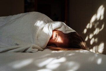 Beautiful, young blonde lies on the bed in the rays of soft, morning sun. Buried under the covers,...