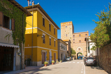 Fototapeta na wymiar A street in the historic medieval village of Paganico near Civitella Paganico in Grosseto Province, Tuscany, Italy. Part of the city walls can be seen at the far end of the street