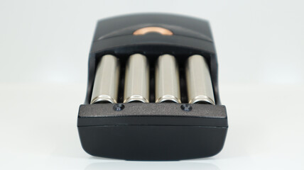 Rechargeable alkaline batteries in a battery charger on a white background. AA fast charger in...
